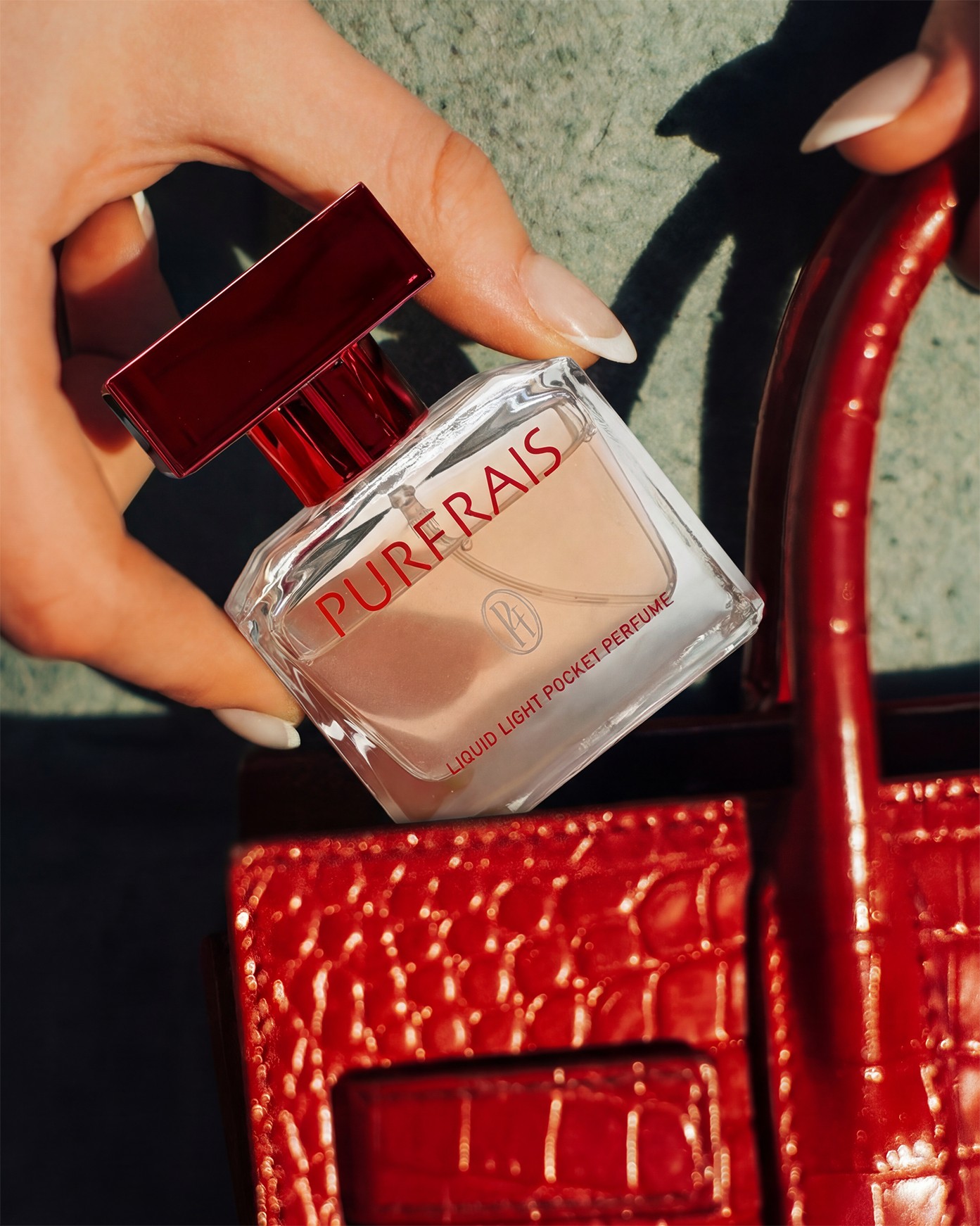 Hand holding a PURFRAIS pocket perfume over a red bag